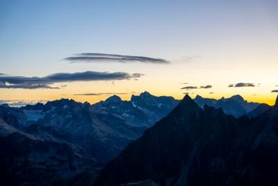 Silhouetted mountain peaks at dusk with a clear sky and scattered clouds above the horizon.