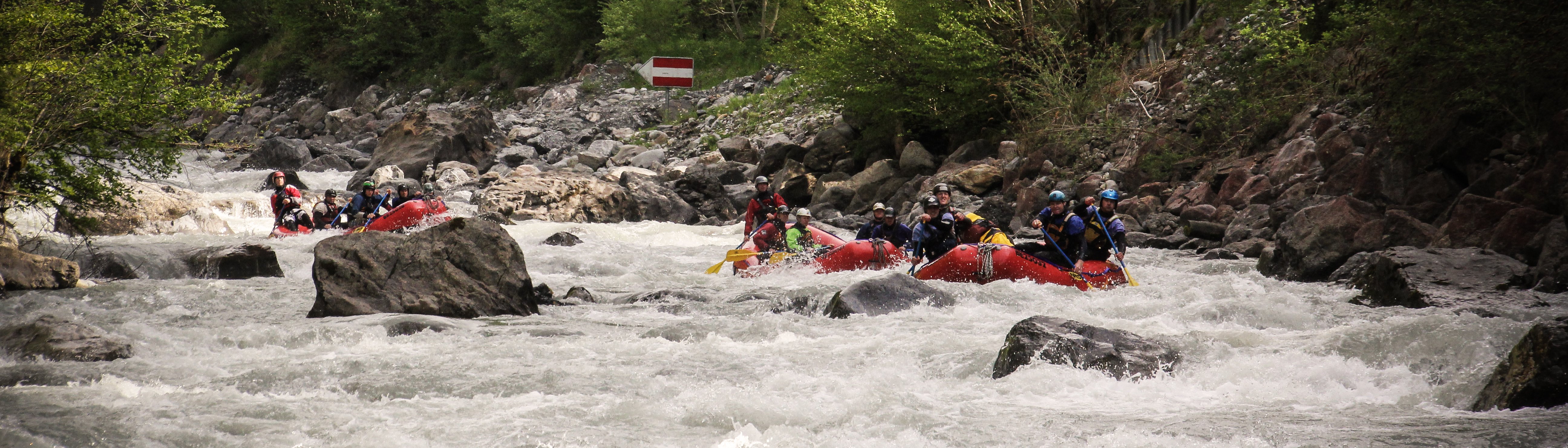 Personen in roten Schlauchbooten beim Rafting auf einem Fluss, mit Helmen und Schwimmwesten.