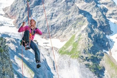 Eine Frau klettert via Selbstaufstieg an einem Seil hoch. Im Hintergrund ist die Gletscherlandschaft zu erkennen.