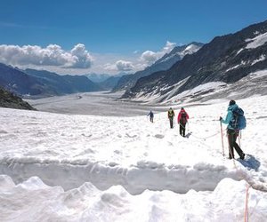 Hikers with backpacks and ropes traverse a snowy mountain landscape under a clear sky.