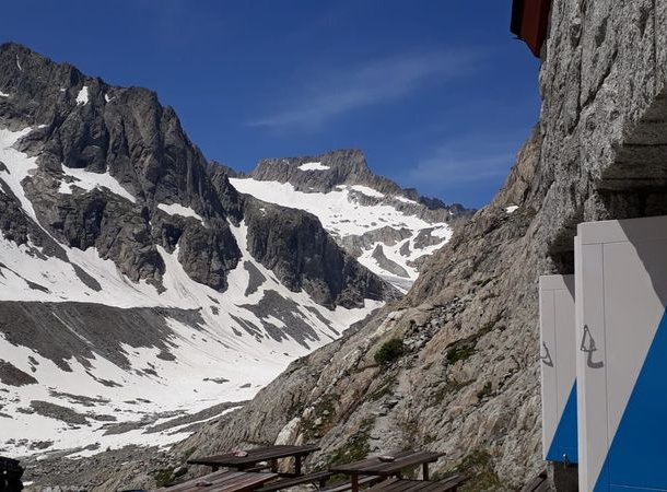 Snow-covered mountains with rocky peaks, adjacent to a stone building and picnic tables.