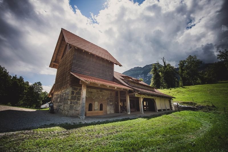 Old wooden building in a rural mountain landscape with cloudy sky in the background.