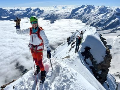 Mountaineer with helmet and climbing gear on a snow-covered ridge in an alpine mountain landscape.