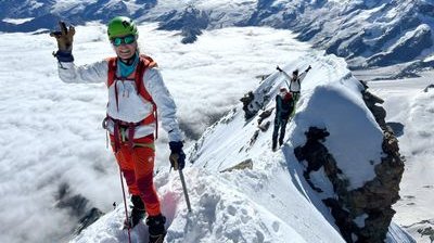 Mountaineer with helmet and climbing gear on a snow-covered ridge in an alpine mountain landscape.