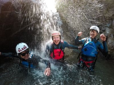 Three people laughing under a waterfall while canyoning in a gorge.