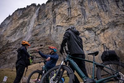 People with helmets and bicycles in front of a steep rock face.