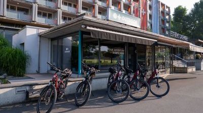 Fahrräder stehen vor einem Gebäude eines Abenteuerunternehmens mit Beschilderung und einem mehrstöckigen Gebäude im Hintergrund.