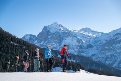 Personen mit Schneeschuhen und Stöcken wandern in einer verschneiten Berglandschaft.