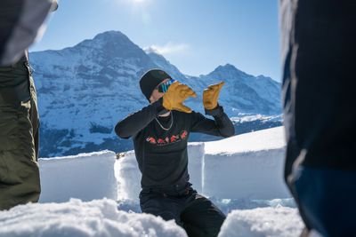 Person in winter clothing with gloves in the snow, surrounded by mountains, building snow blocks.