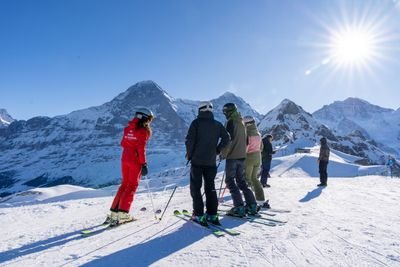 Personen mit Skiern und Helmen stehen auf schneebedecktem Berg, umgeben von Alpenlandschaft.
