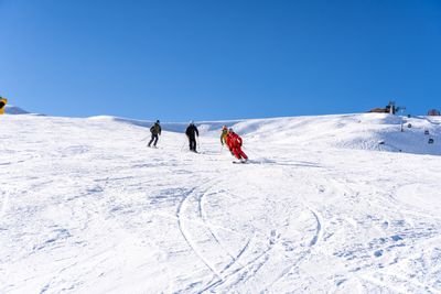 Three people skiing down a snow-covered slope, with a blue sky in the background.