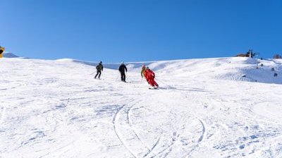 Three people skiing down a snow-covered slope, with a blue sky in the background.
