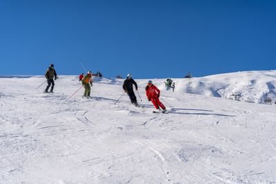 Several people are skiing with helmets on a snow-covered slope in the mountains.