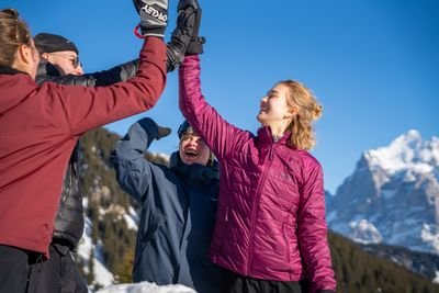 People in winter clothing are giving each other high-fives in a snowy mountain landscape.