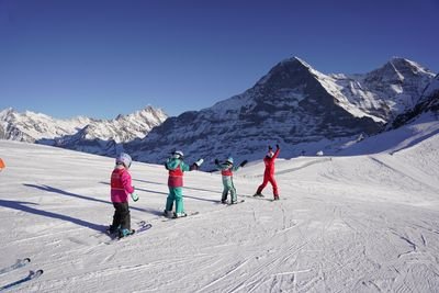 People in ski gear on a slope in the mountains, wearing helmets and ski poles.