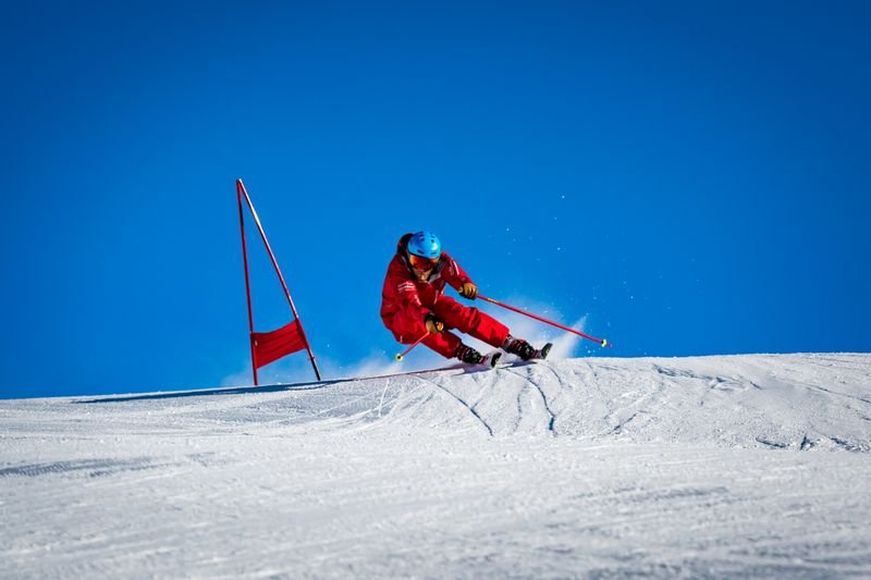 Skier in red clothing with a helmet is skiing on a snow-covered slope next to red gate poles.