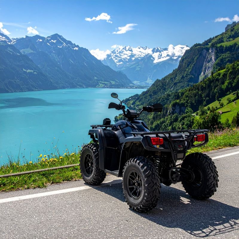 Geländefahrzeug (ATV) steht auf Bergstraße mit Blick auf See, Berge und schneebedeckte Gipfel.