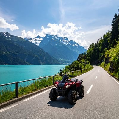 Rotes Quadfahrzeug auf asphaltierter Straße entlang eines türkisfarbenen Sees mit Bergen und Schnee im Hintergrund.