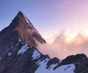 Snow-covered mountain peak with clouds at sunrise, clear sky in the background.