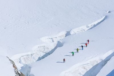 Group of mountaineers with helmets and ropes crossing a snow-covered glacier in the Alps.