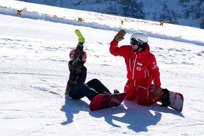 Two people in snowboarding gear high-five on a snowy mountain slope, wearing helmets and goggles.