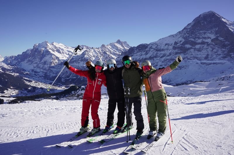 Four people in ski gear posing on a snowy slope with a mountain backdrop.
