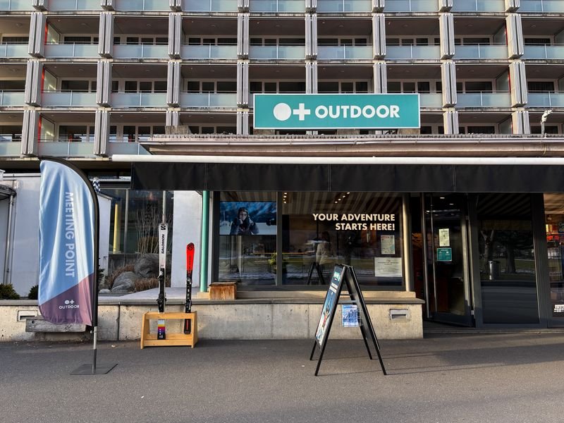 Außenansicht eines Outdoor-Abenteuerladens mit Skiern und Werbebanner vor dem Eingang.