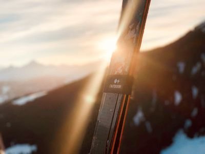 Ski vor Berglandschaft bei Sonnenuntergang, Schnee auf den Gipfeln sichtbar.