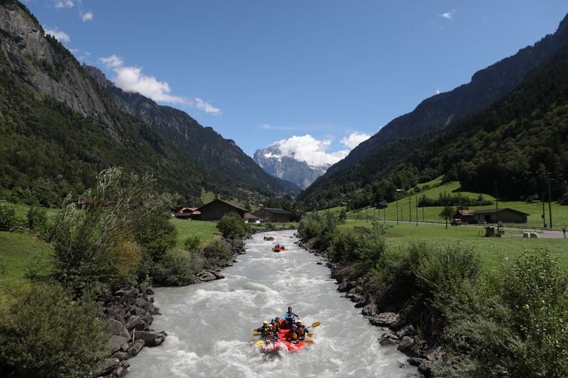 People in an inflatable boat rafting on a river in an alpine valley with mountains.