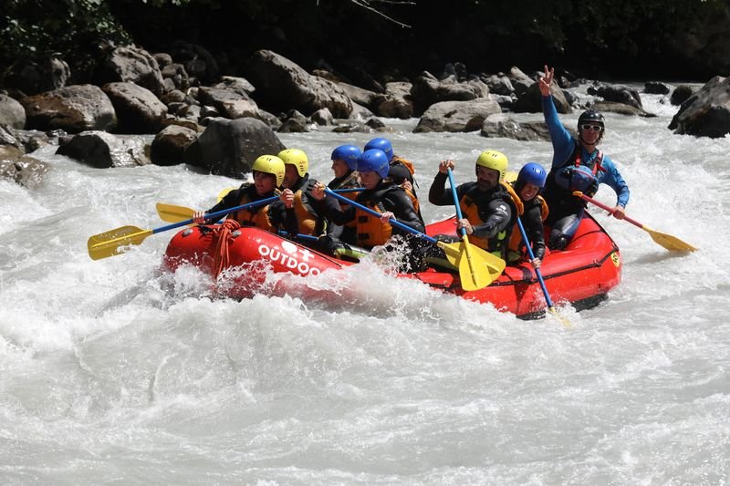 People in helmets and life jackets rafting on a river in a red inflatable boat.