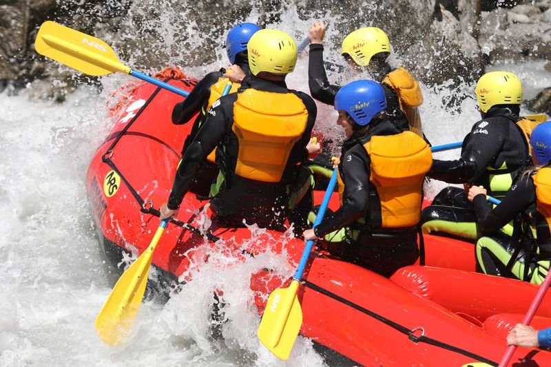 People in wetsuits and helmets rafting on a whitewater river in the mountains.