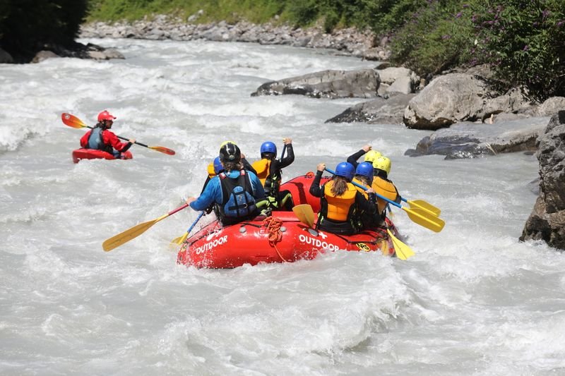 People in helmets and life jackets are rafting in a red boat on a river in the mountains.