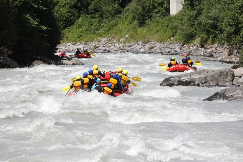 People in inflatable boats with helmets and life jackets rafting on a river in the mountains.
