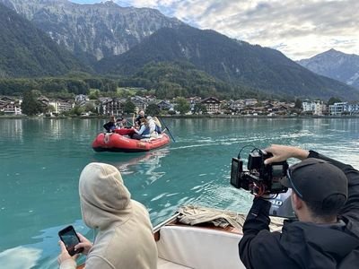 People in an inflatable boat on a lake, surrounded by mountains, with camera shots from the boat.