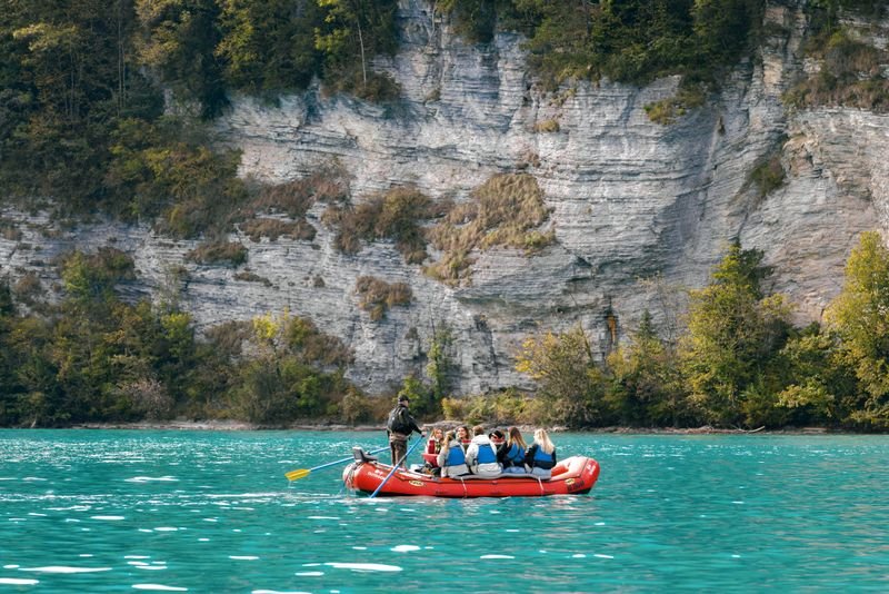 People in an inflatable boat on a turquoise lake, surrounded by rocks and trees.