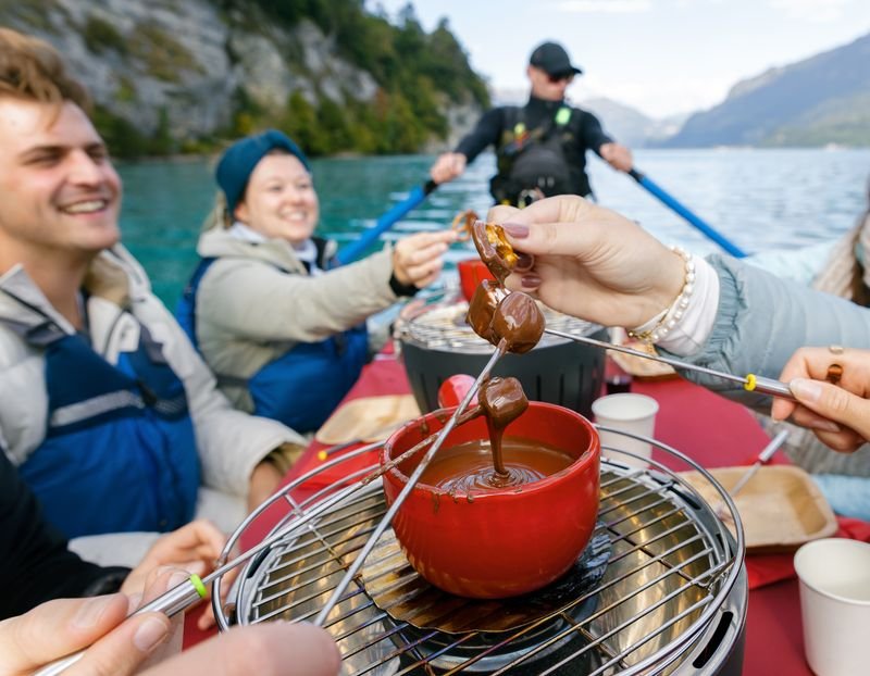 People in a boat on a lake are enjoying chocolate fondue; they are wearing life jackets.