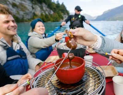 People in a boat on a lake are enjoying chocolate fondue; they are wearing life jackets.