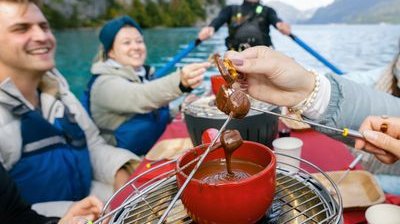 People in a boat on a lake are enjoying chocolate fondue; they are wearing life jackets.