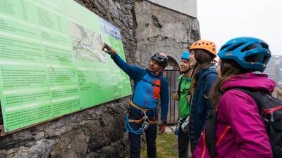 Bergführer zeigt auf Informationstafel am Start des Klettersteig Mürren