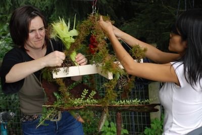 Two people are creating a decorative object with plants outdoors.