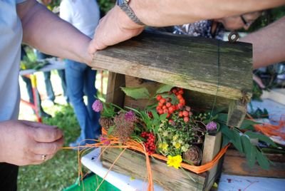 People are decorating a wooden birdhouse with colorful flowers and berries on a table outdoors.