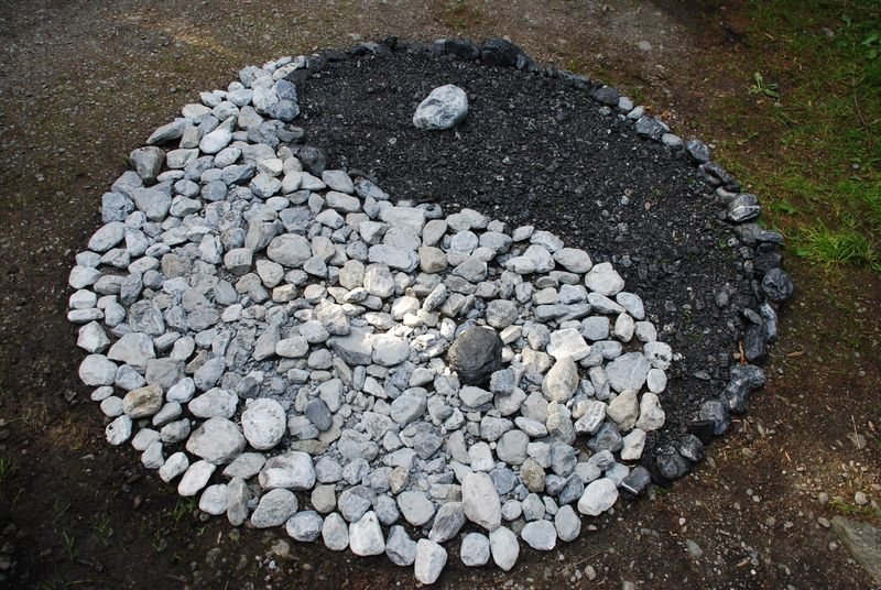 Stone pattern in the shape of a Yin-Yang symbol on the ground, surrounded by grass.