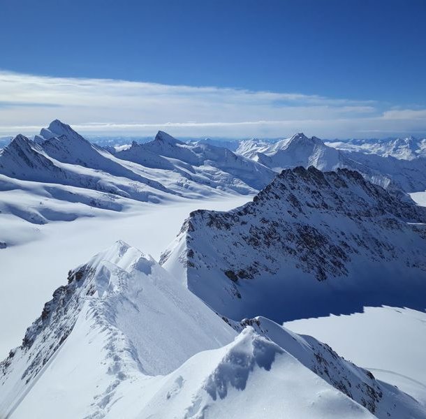 Snow-covered mountain peaks under a clear blue sky in a vast alpine landscape.