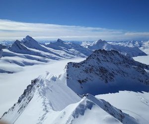 Snow-covered mountain peaks under a clear blue sky in a vast alpine landscape.