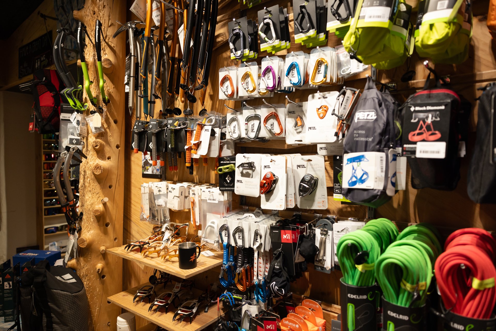Kletterausrüstung und Seile in einem Geschäft; Helme, Karabiner und Gurte an der Wand ausgestellt.