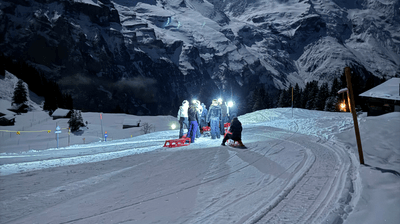 People with sleds and headlamps on a snowy mountain path at night, with mountains in the background.