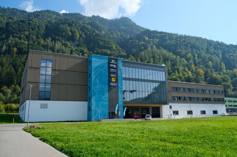 Modern building with a blue facade in front of wooded mountains and green lawn in Switzerland.
