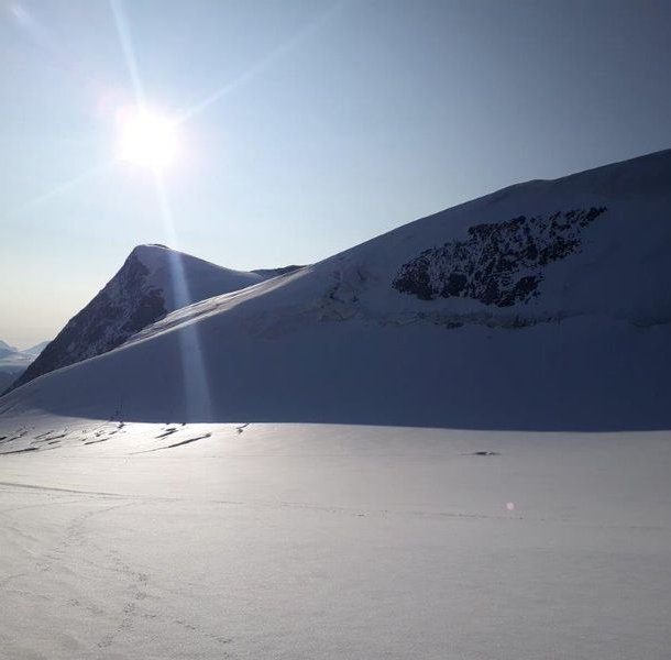 Snow-covered mountain landscape with sunlight shining over peaks, casting shadows on the snow.
