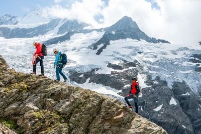Eine Gruppe von Bergsteiger*innen geht über einen Grat. Im Hintergrund ist die vergletscherte Bergwelt zu erkennen.