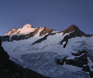Snow-covered mountain peaks at dusk with a clear sky backdrop.